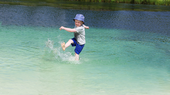 Small boy with a blue sun hat playing on a fresh water sandy beach in a Vacation resort in Ireland