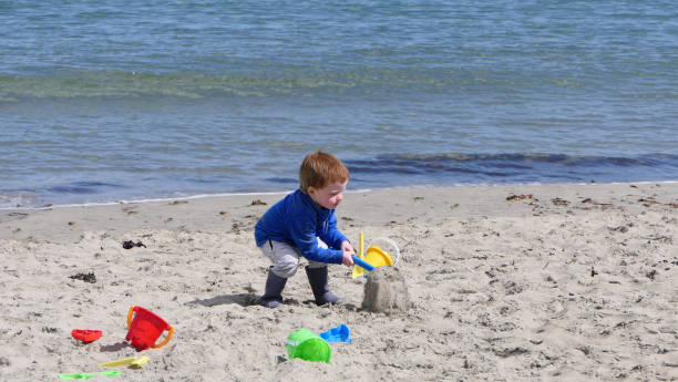 istock Red headed boy playing with Bucket spade and Digger on sandy beach 1953879175
