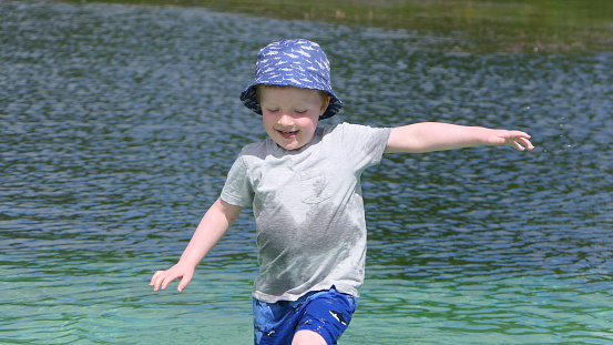 Close-up of a two year old boy holding Dad's hand as he stands in the water at the beach with his family.