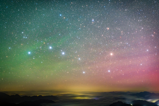 The advection fog of the city and the Big Dipper in the sky, with green and red hues floating in the sky, create a dreamlike starry sky.Hami, Xinjiang, China\n\n.