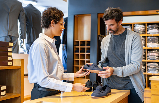 Latin American man buying shoes at a menâs clothing store with the help of a retail clerk
