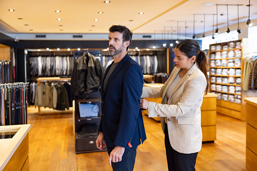 Latin American man trying on a suit at a clothing store with the help of a seamstress - menswear concepts