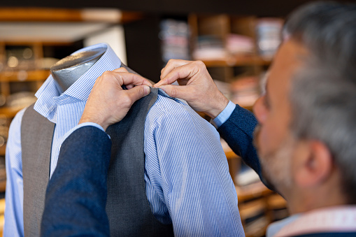 Close-up on a tailor stitching clothes on a mannequin at his shop - menswear concepts