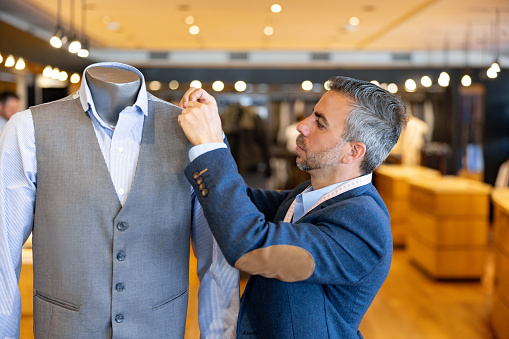 Latin American tailor stitching clothes on a mannequin at his shop - menswear concepts