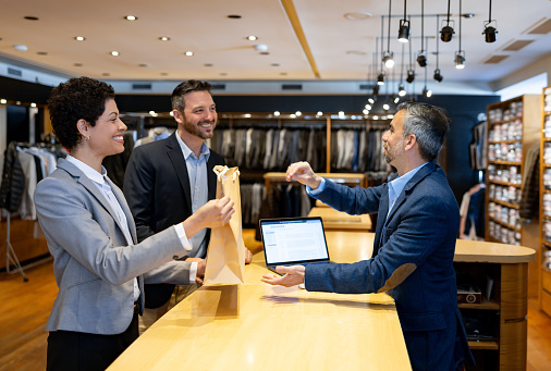 Happy Latin American couple shopping at a clothing store and receiving a bag at the counter while smiling