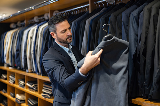 A young Caucasian man is standing in a clothing store and checking out a jacket with a smile on his face.