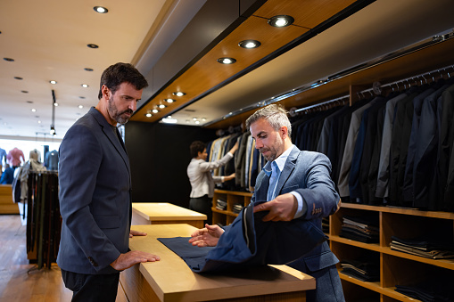 Elegant Latin American man buying pants at a clothing store with the help of a retail clerk - shopping concepts
