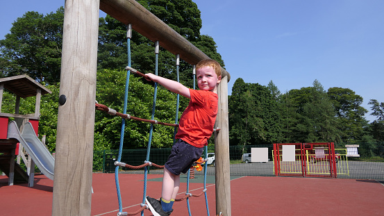 Red headed boy with a red t-shirt having fun having fun in a Playpark on a sunny day