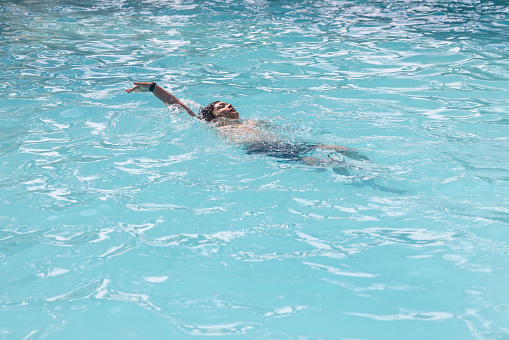 Mixed race boy performing the backstroke in a outdoor pool.