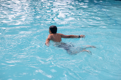 Mixed race boy performing the butterfly swimming stroke in a outdoor pool.