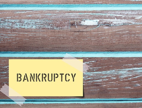 Yellow sticky note on wood wall with text BANKRUPTCY -  legal process when one cannot repay debts to creditors and seek relief from some or all debts - imposed by court order.