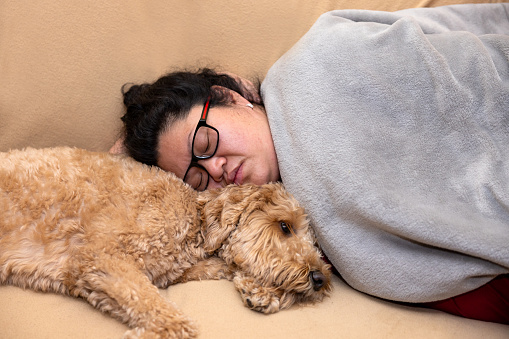 Woman of Asian decent napping with a Goldendoodle dog.