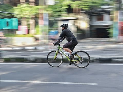 Bandung, Indonesia - December 19, 2021 : Male cyclist riding through Dago Street, Bandung, Indonesia. He is wearing cycling gear, going for a training ride or commuting in style, on a sunny day.