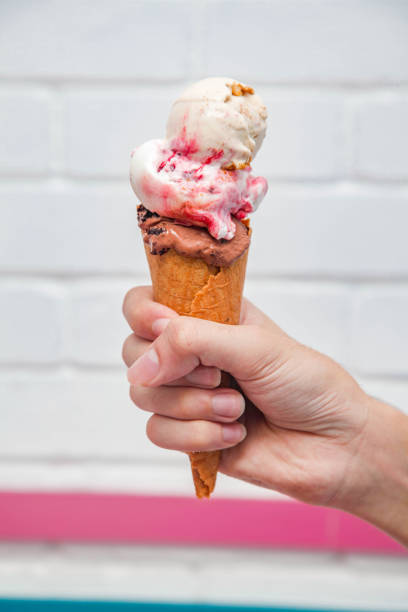 istock Gelato waffle cone ice cream holding in hand with white bricked background. 1954018249
