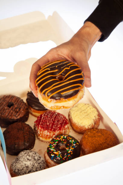 istock Hand holding a doughnut out from the box of assorted donuts. 1954018263