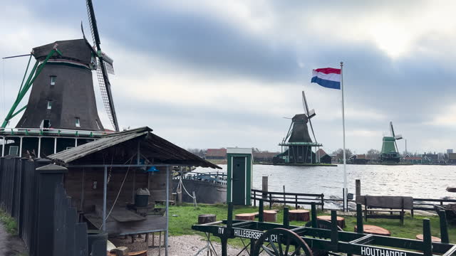 Traditional windmill and dutch flag in Zaanse Schans in the Netherlands, dutch flag with windmills in the Netherlands, ancient wooden windmills in Zaanse Schans, most popular tourist attraction in the Netherlands, dutch national flag
