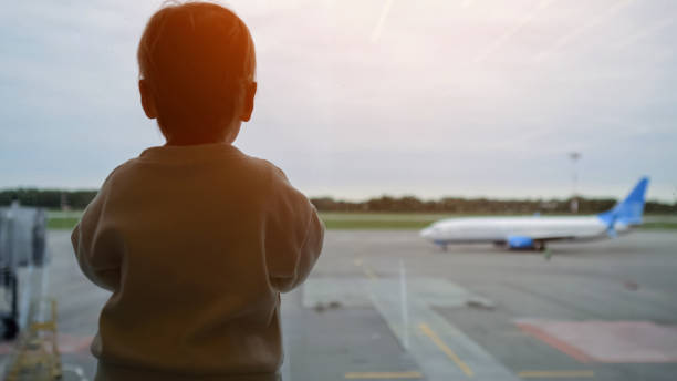 istock Child stands looking through window at taking off plane 1954062296