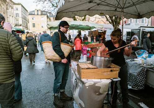 December 23, 2023, Cahors, France:Locals and tourists enjoying food and drinks and buying local produce at the weekend market. Street markets in Cahors are held every Wednesday and Saturday. Local people and tourists come along to buy local produce on the bustling stalls.