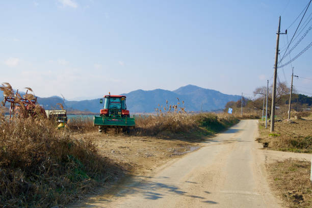 Sangju City, South Korea - November 18th, 2023: A tractor and other farm equipment parked near the Nakdong River bike path, with power lines and rural mountains in the background.