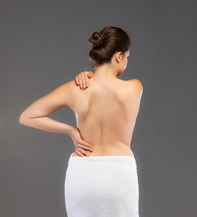 Woman massaging back pain on grey background.  “Image is not body shape retouched”