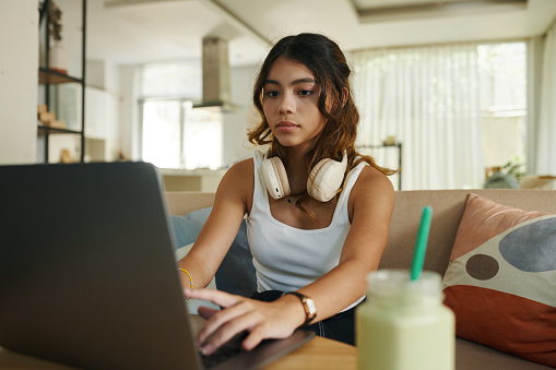 Serious teenage girl with headphones working on laptop
