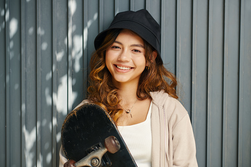 Portrait of happy girl in bucket hat holding skateboard