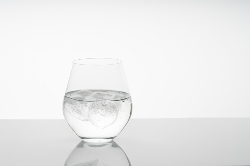 Fresh drinking water in a beautiful rounded glass with ice on on reflective table