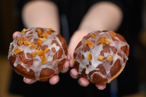 The girl holds in her hands two sweet donuts with jam, icing and candied orange peel close up isolated