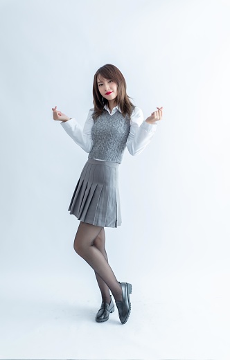 Asian school girl in grey skirt and white blouse posing with hands in heart shape