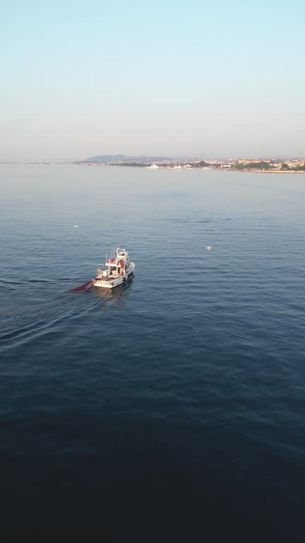 Aerial view of a fishing boat setting the fishing net. A seagull flies around the boat. Camera is rotating around the boat.