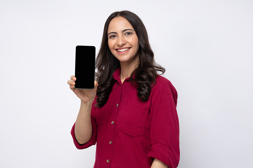 Photo of beautiful happy smiling young woman wearing shirt standing isolated over white background showing mobile phone with blank screen