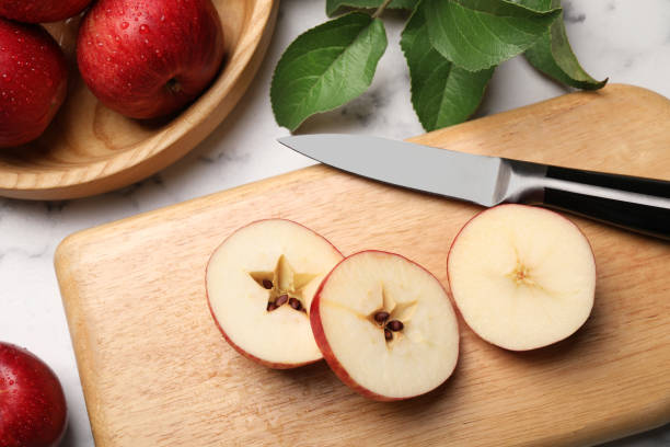 istock Cut red apple, knife and green leaves on white marble table, above view 1954234279