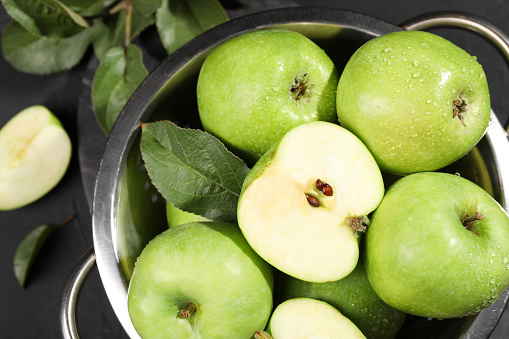 Ripe green apples with water drops and leaf in colander on table, top view