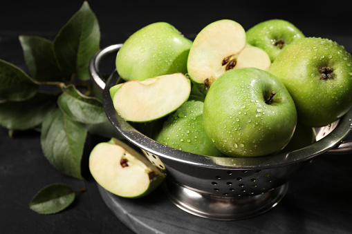 Ripe green apples with water drops and leaves on black table, closeup