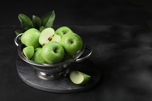 Ripe green apples with water drops and leaves on black table, space for text