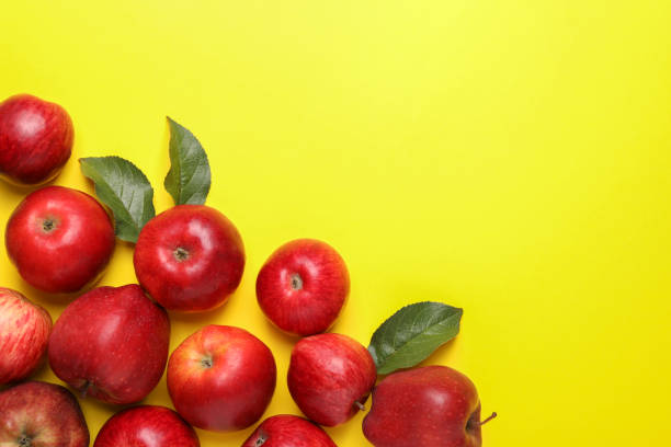 istock Ripe red apples and green leaves on yellow background, flat lay. Space for text 1954236419