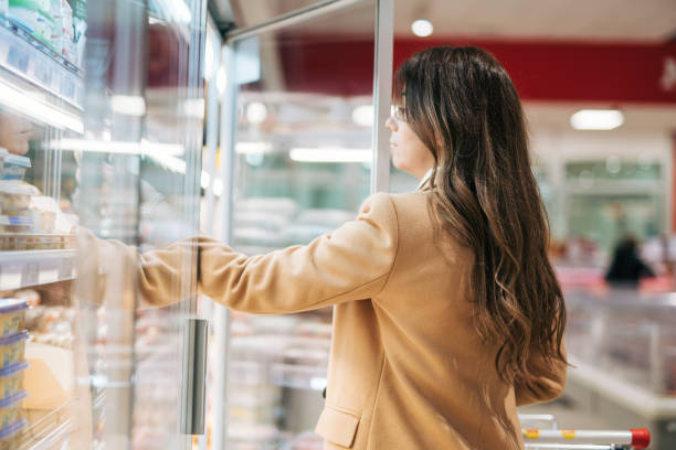 piękna kobieta z wózkiem otwiera lodówkę w supermarkecie i wybiera, co kupić - chłodnictwo zdjęcia i obrazy z banku zdjęć