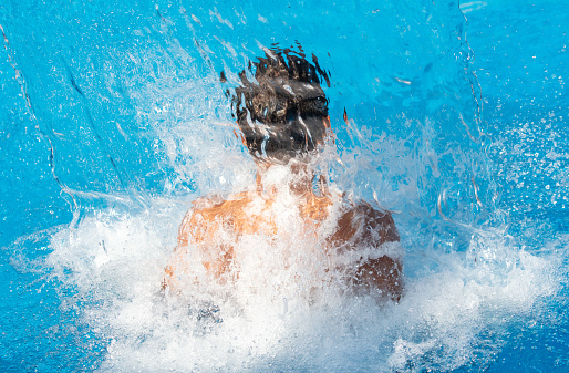 A boy stands under splashes of water in the pool.