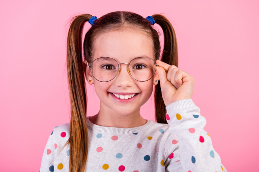 Portrait of clever good mood schoolgirl with ponytails hairdo dressed dotted pullover touching eyewear isolated on pink color background.
