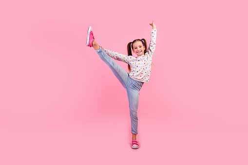 Full size photo of talented schoolgirl dressed dotted pullover denim pants dancing hold leg hand up isolated on pink color background.