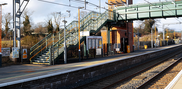 Railway tracks and platforms at Hooton Station in Wirral in north-west England, UK. A single commuter train waits at the platform for commuters to alight and board the train.