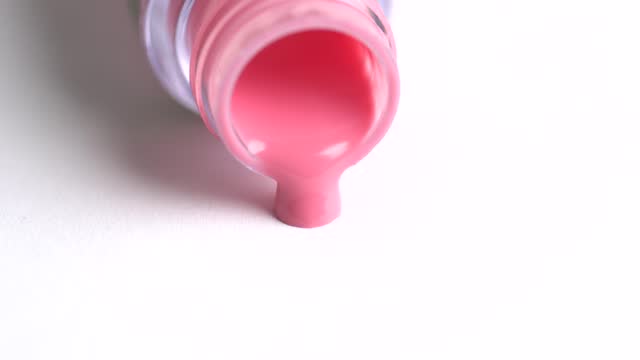 Pink lipgloss flows out of an overturned bottle. Coral lipgloss pouring on white background. Advertising concept for decorative cosmetics