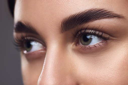 Close-up of a woman's eyes with well-defined eyebrows, full lashes, and smooth skin, highlighting meticulous grooming. Concept of beauty, eyebrow shaping kit, grooming and natural brow look.