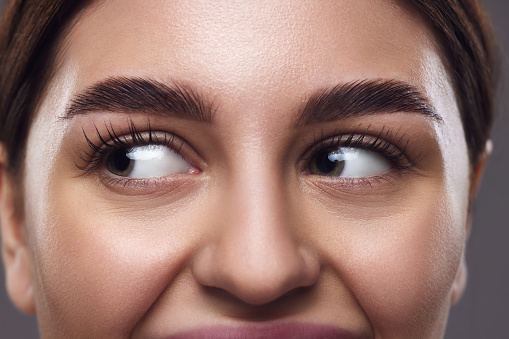 Close-up of female face, eyes with well-groomed eyebrows, clear eyes, and smooth skin against neutral grey background. Concept of medical, techniques for vision, and focusing for eyes. Ad