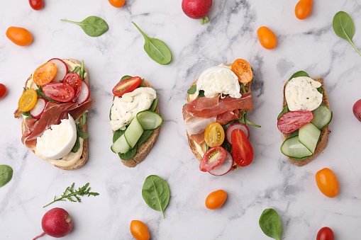 Delicious burrata sandwiches served on white marble table, flat lay