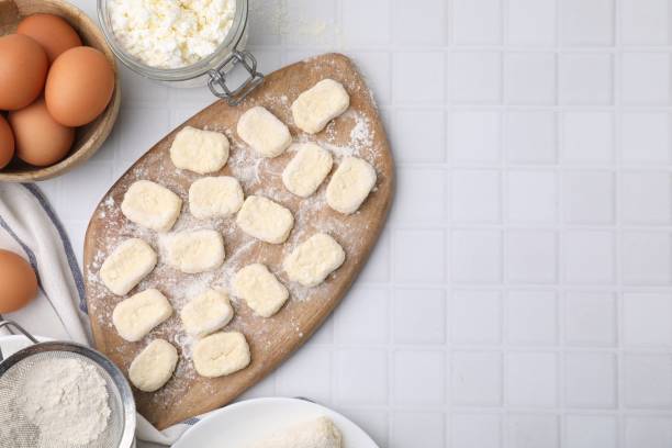 istock Making lazy dumplings. Board with cut dough and ingredients on white tiled table, flat lay. Space for text 1954297514