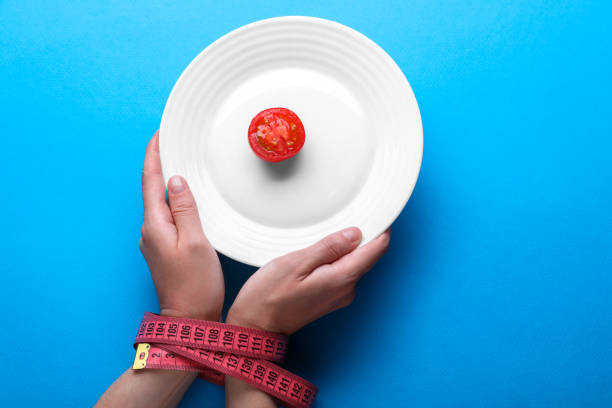 mulher segurando o prato com tomate cereja nas mãos amarradas com fita métrica no fundo azul claro, vista superior. conceito de dieta - plate blue loss tape measure - fotografias e filmes do acervo