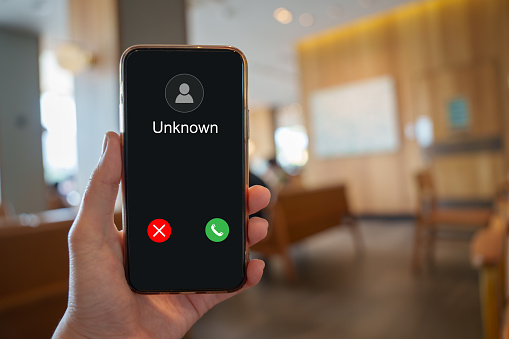 Unknown call. Person holding mobile phone and screen showing Unknown caller from scam, fraud or phishing. Information security terms cybersecurity concept.