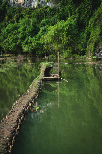 Traditional wooden boat in river along sunny green grown lush karst mountains, Ninh Binh, Vietnam