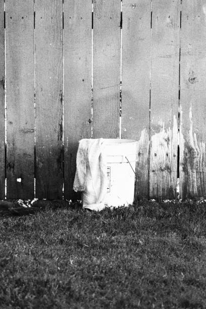 A white bucket in the middle of a fence & on grass.